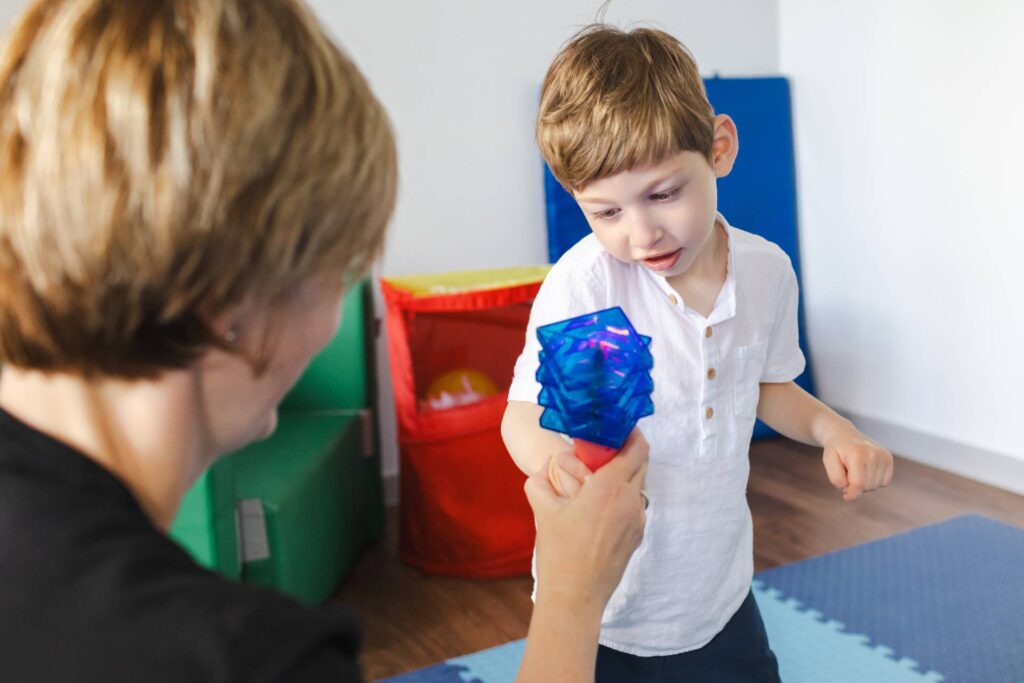 Physical therapist helps a young boy with cerebral palsy during a playful rehabilitation session, using colorful tools to encourage movement